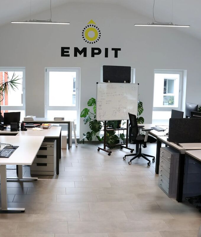 One of the modern open-plan offices in Berlin filled with white desks arranged in clusters, each topped with multiple computer monitors, laptops, and piles of documents.