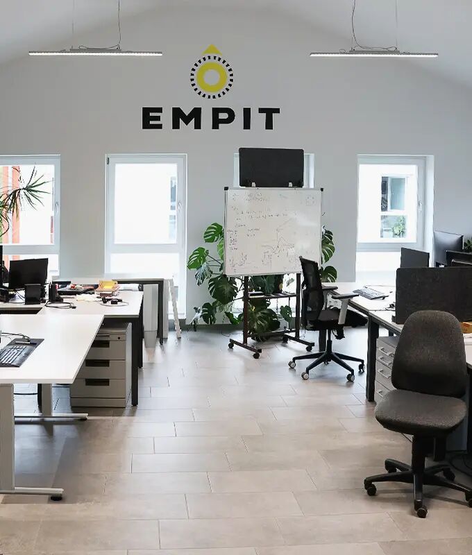 One of the modern open-plan offices in Berlin filled with white desks arranged in clusters, each topped with multiple computer monitors, laptops, and piles of documents.