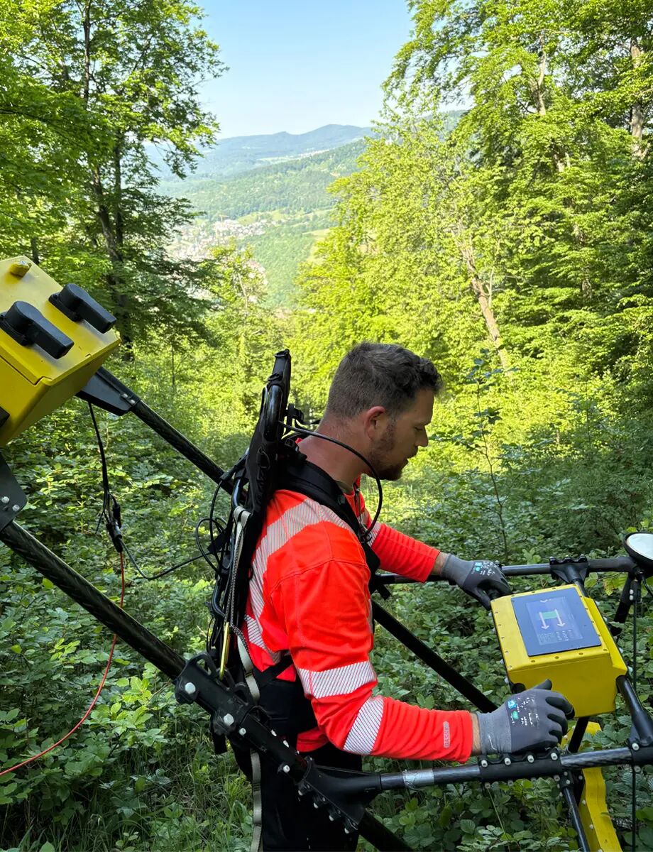 Inspector with the hand held device inspects in front of a green forest area with thick vegetation.