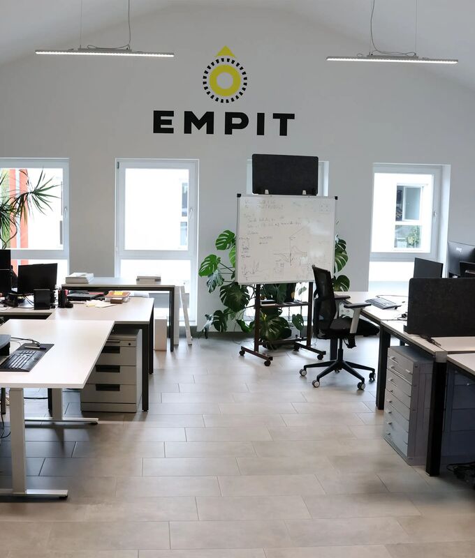One of the modern open-plan offices in Berlin filled with white desks arranged in clusters, each topped with multiple computer monitors, laptops, and piles of documents.
